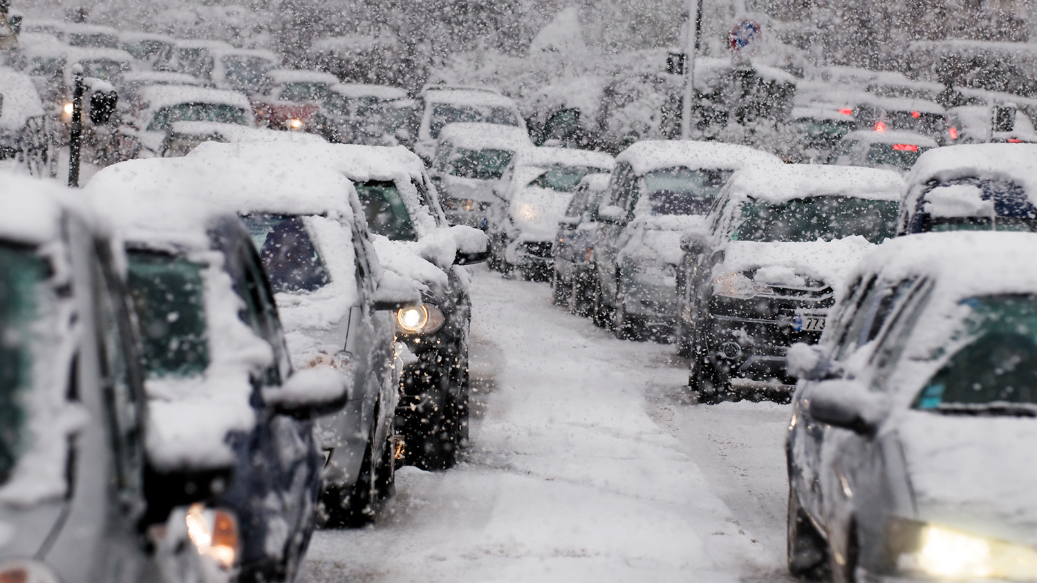 Filas de carros, cobertos de neve, esperam em estradas cobertas de neve.